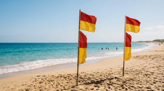 Red and yellow safety flags marking patrolled swimming area on Australian beach with crystal clear turquoise water