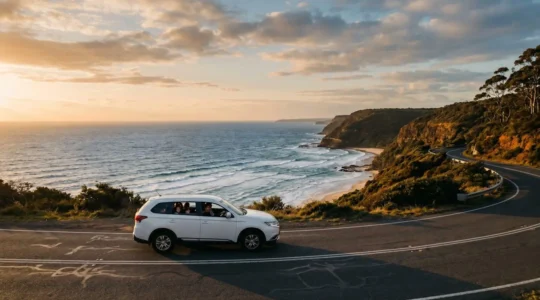 Family car driving along scenic Australian coastal highway with ocean views and children visible through windows