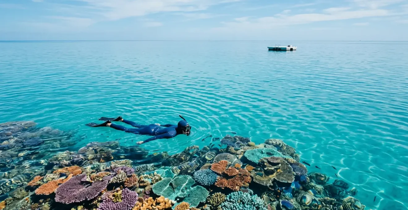 Snorkeler floating above vibrant coral reef with calm turquoise water and empty pontoon in distance