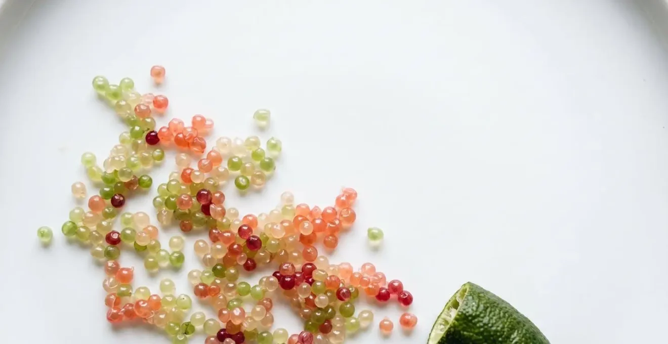 Wide minimal composition showing finger lime caviar pearls scattered on a clean white surface with negative space