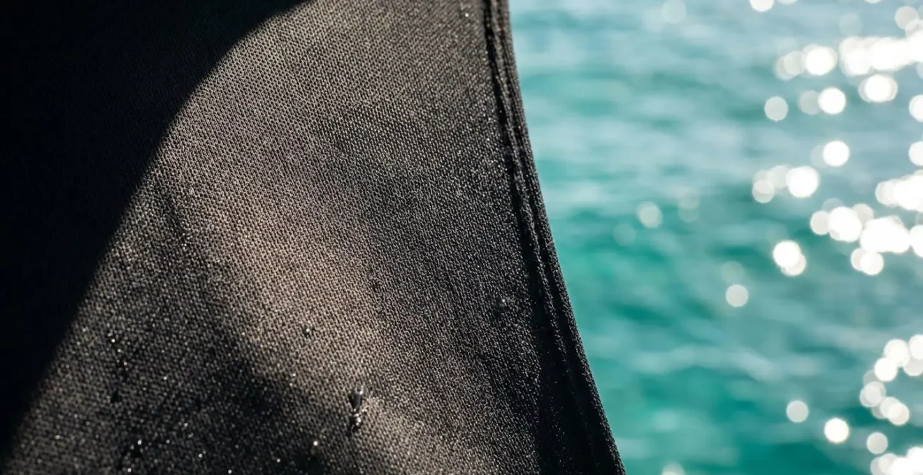 Close-up detail of black lycra stinger suit fabric showing tight weave pattern against tropical water background