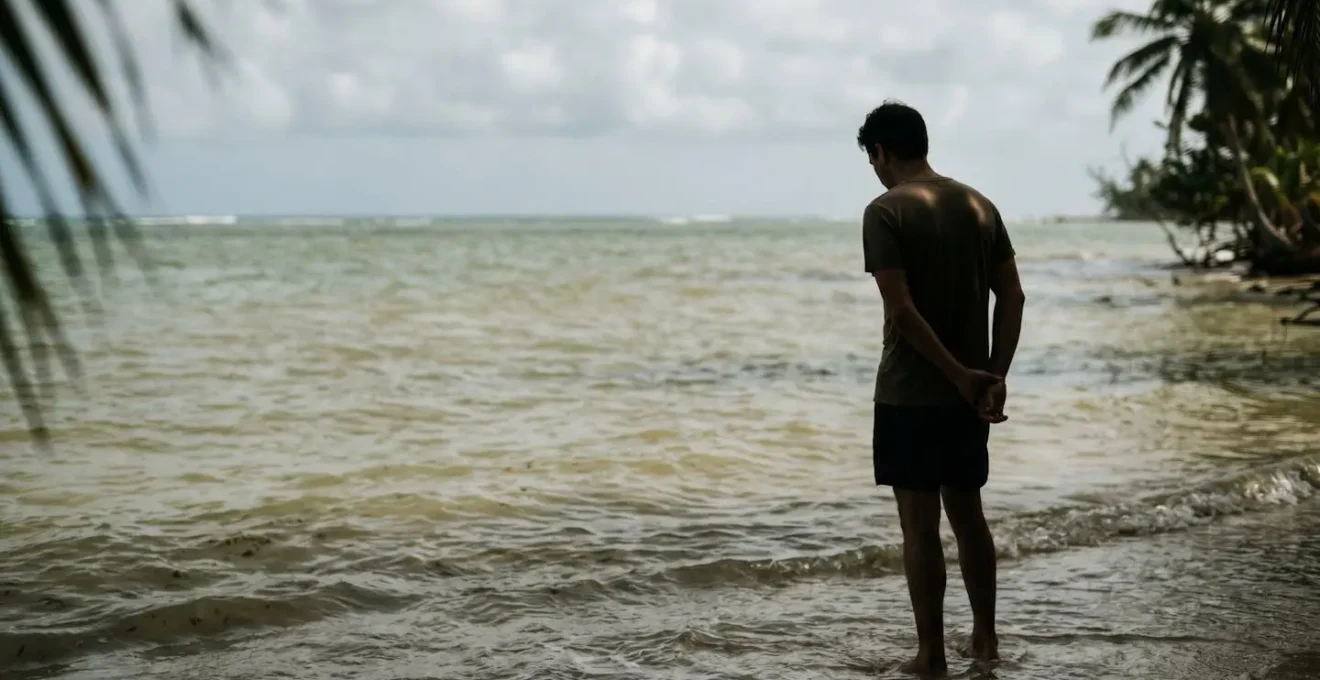 Person standing at edge of tropical beach with cloudy post-storm water, contemplating swimming safety in stinger season with murky visibility